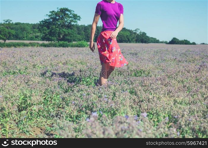 A happy young woman is spinning around in a field of purple flowers on a sunny summer day