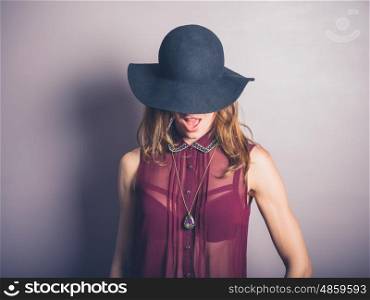 A happy young woman wearing a hat and a see through shirt is smiling