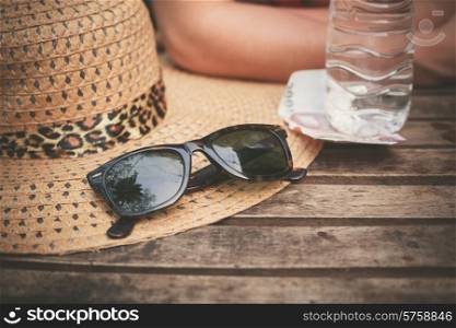 A hat and a pair of sunglasses on a table outside with a woman in the background