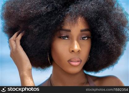 A head shot of a sensual looking attractive young black female with gorgeous makeup and a beautiful Afro posing by herself outside during a sunny day.