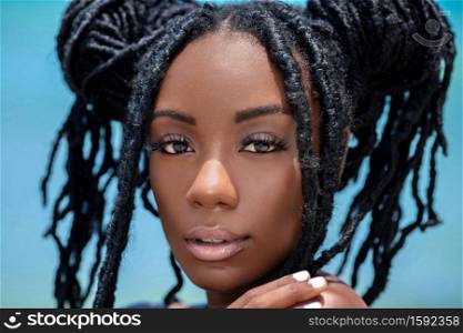 A head shot of a sensual looking attractive young black female with beautiful makeup & long dreadlocks posing by herself on a sunny summer day at a tropical beach.