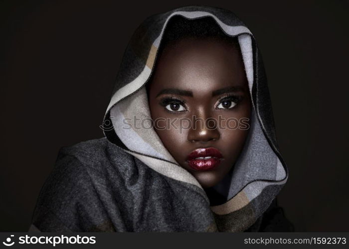 A headshot of a cute young black female with short black curly hair, beautiful makeup and vibrant red lip stick wearing a colorful head scarf in front of a black background.