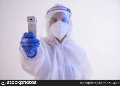 A health worker in PPE kit holding a temperature checking gun.