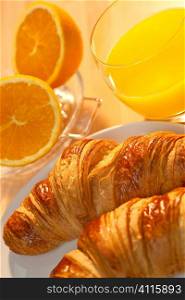 A healthy continental breakfast of croissant pastries, orange juice, oranges Illuminated with golden early morning sunshine.