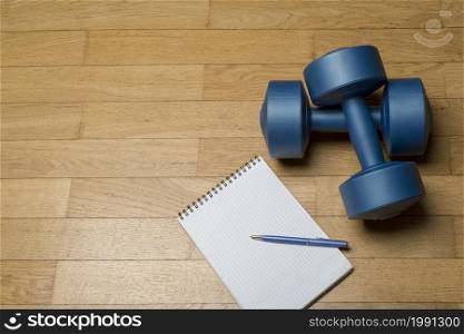 A healthy mind in a healthy body. A paper notebook and a dumbbell on a wooden floor. The concept of a healthy lifestyle, fitness.. A healthy mind in a healthy body. A paper notebook and a dumbbell on a wooden floor.
