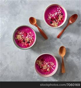 A healthy smoothie made from beets, raspberries, currants and oatmeal in plates with wooden spoons on a gray concrete background with copy space. Top view. Beetroot smoothies. Three plates with a diet breakfast with wooden spoons on a gray concrete background. Top view