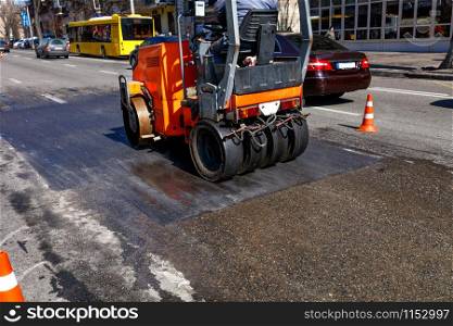 A heavy orange vibratory roller compacts and levels a section of road on a city street fenced with traffic cones, image with copy space.. Vibrating orange road roller repairs the road section on a city street.