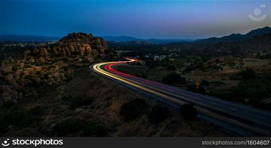 A high angle shot of yellow and red lights on the highway surrounded by rocks at night. High angle shot of yellow and red lights on the highway surrounded by rocks at night