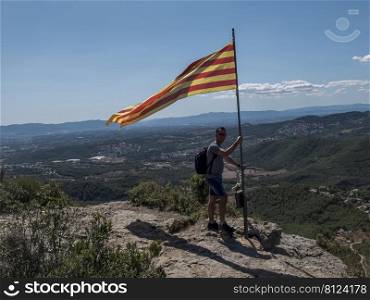 A hiker man holding and waving Catalonia flag on top mountain