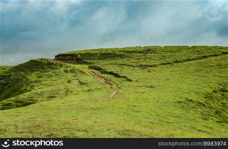 A hill surrounded by other green hills, A path to a green hill with blue sky with copy space