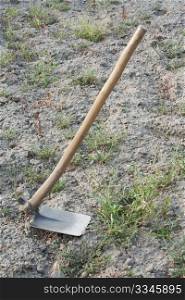 A hoe (garden tool) with land and weeds as a background.