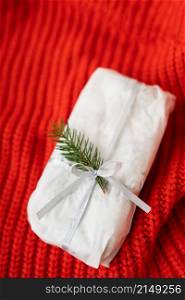 A homemade Christmas stollen sealed in white craft paper lies on a red knitted fabric. Gift wrap. A homemade Christmas stollen sealed in white craft paper lies on a red knitted fabric. Gift wrap.