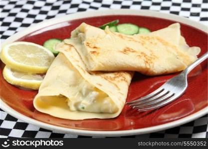 A homemade crepe filled with chicken in white sauce, served with slices of lemon and cucumber.