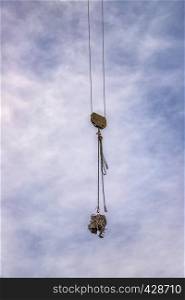 A hook of a crane with load at the blue sky with clouds as a background. Vertical view
