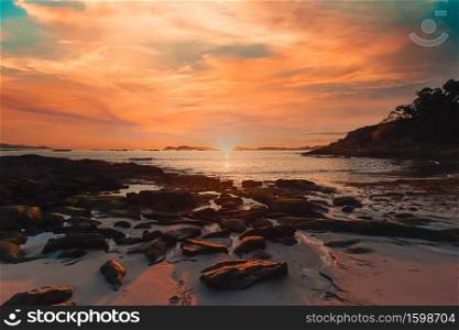 A horizontal image of a tide on the beach over the sand during a colorful sunset with the islands as the background and copy space