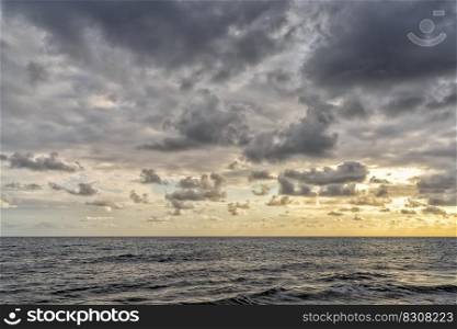 A horizontal landscape view of a backdrop of calm ocean water under an expressive and cloudy sky