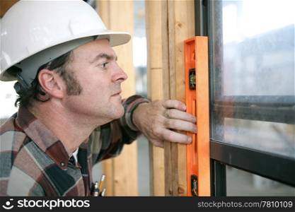 A horizontal view of a carpenter checking a newly installed window to see if it&rsquo;s level. Authentic and accurate content.