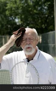 A hot and tired senior man wiping his brow after a tennis match.