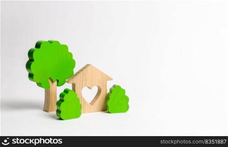 A house with a heart and wooden figures of trees with bushes. The concept of a love nest. Acquisition of affordable housing in a mortgage or loan. Accommodation for young families. Romantic gift.