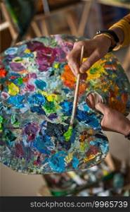 A huge palette in the hands of the artist at work.. The artist holds a palette in her hand and mixes colors 2877.