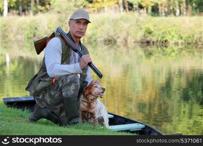A hunter and his dog by a river.