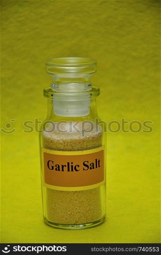A jar filled with garlic salt on a yellow background