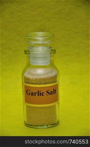 A jar filled with garlic salt on a yellow background
