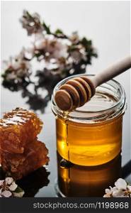 A jar of honey with honeycombs and a stick on a light background