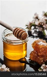 A jar of honey with honeycombs and a stick on a light background