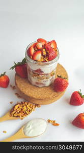 a jar with tasty parfaits made of healthy granola, strawberries and Greek yogurt on white background. Shot at angle.