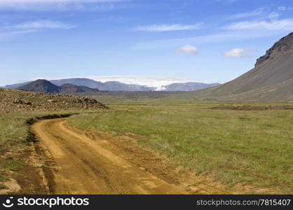 A jeep track or dirt road in Iceland leading around the Hlodufell Volcano winding around remnants of volcanic eruptions, with a clear view of the Langjokull glacier in the distance