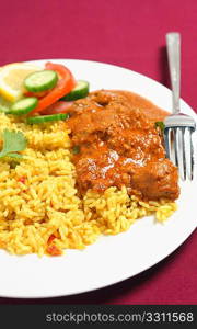 A kashmiri lamb curry with rice and a fork on a plate ove a maroon tablecloth.