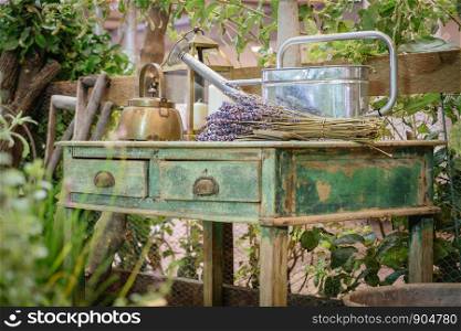 A kettle, watering can and lavender flowers bunch on old style wooden green table. Cottage outdoor garden rustic country style decoration. Selective focus.