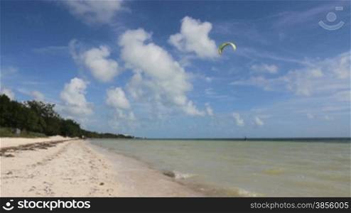 a kite surfer hangs onto his kite in the water at a beautiful beach