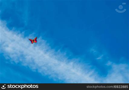 A kite that resembles a butterfly hovers in the blue sky.