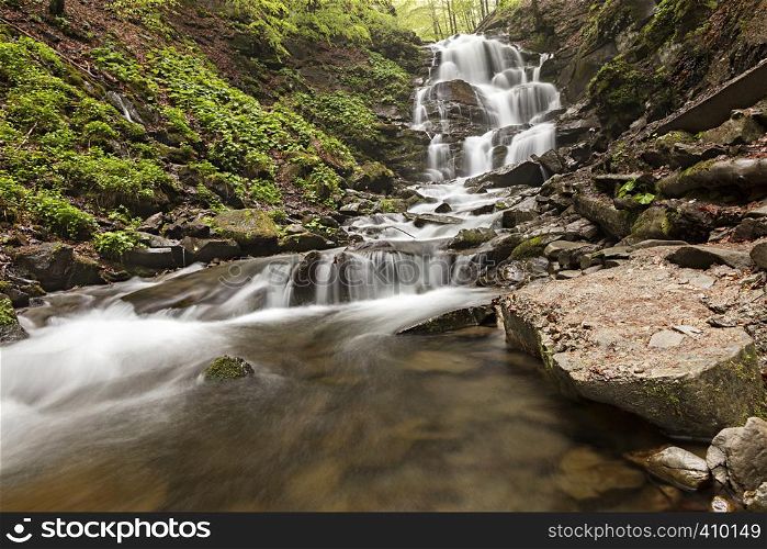 A large boulder washed early in the morning at the foot of a waterfall in the Carpathian Mountains. A large boulder lies at the foot of a waterfall in the Carpathian mountains