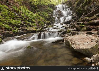 A large boulder washed early in the morning at the foot of a waterfall in the Carpathian Mountains. A large boulder lies at the foot of a waterfall in the Carpathian mountains