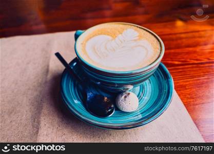 A large cup of cappuccino stands on a saucer, it is served on a sheet of Kraft paper in the cafeteria. On a saucer there is a spoon and a small marshmallow cake. Copyspace is over the saucer.. Green cup of cappuccino stands on a saucer, it is served on a sheet of Kraft paper in the cafeteria. On a saucer there is a spoon and a small marshmallow cake.