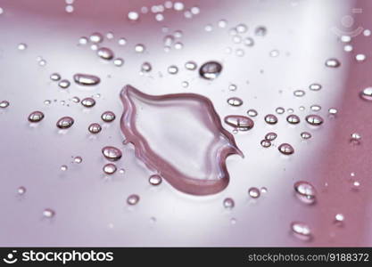 A large drop and splashes of micellar water on a pink background.