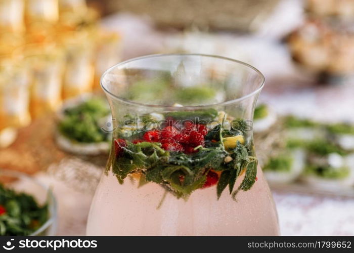 A large glass jugs full of lemonade stands on a light table. In a jug slices of fruit, orange, lemon, grapefruit, raspberry, mint. celebrating party.. A large glass jugs full of lemonade stands on a light table. In a jug slices of fruit, orange, lemon, grapefruit, raspberry, mint. celebrating party