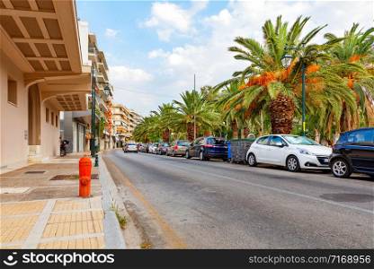 A large number of cars clutter the pedestrian sidewalks of a narrow street in the early morning under the shade of green trees, image with copy space.. The pedestrian part of the road is blocked by parked cars along the road on a narrow city street in the early morning.