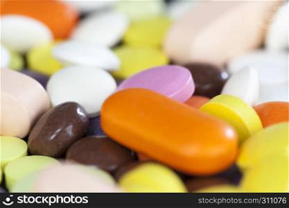 A large number of multi-colored tablets and pills lying together in a chaotic manner. scattered on the surface, closeup photo. multi-colored tablets and pills