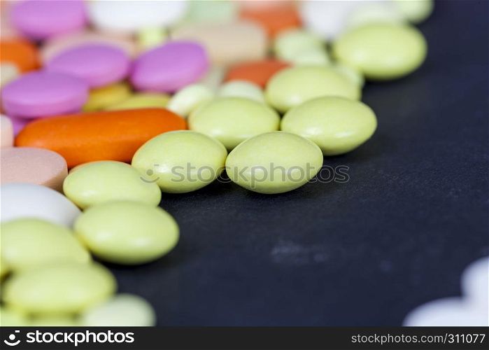 A large number of multi-colored tablets and pills lying together in a chaotic manner. scattered on the surface, closeup photo on a black surface. multi-colored tablets and pills