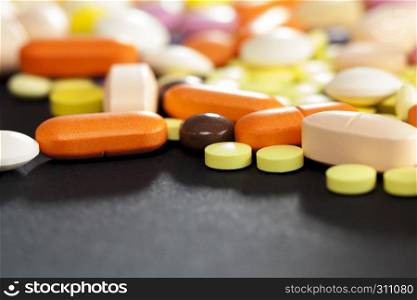 A large number of multi-colored tablets and pills lying together in a chaotic manner. scattered on the surface, closeup photo on a black surface. multi-colored tablets and pills