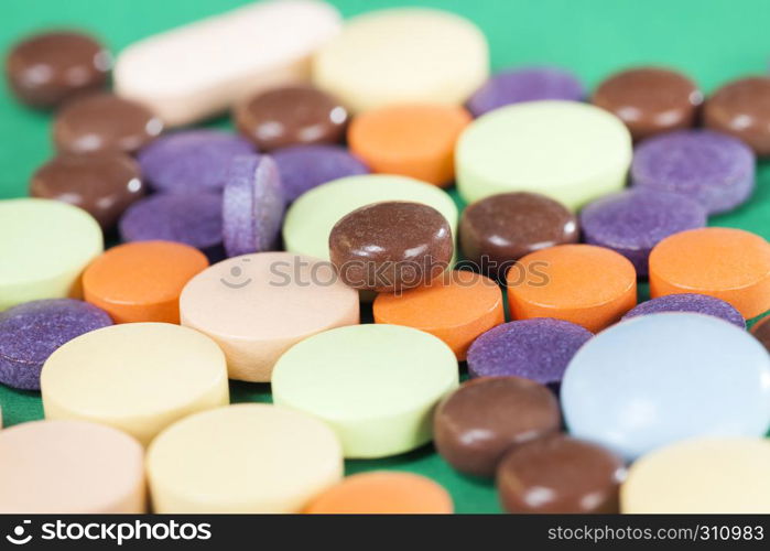 A large number of multi-colored tablets of different forms and purposes with different medical properties lying together in a heap on a green background. multi-colored tablets