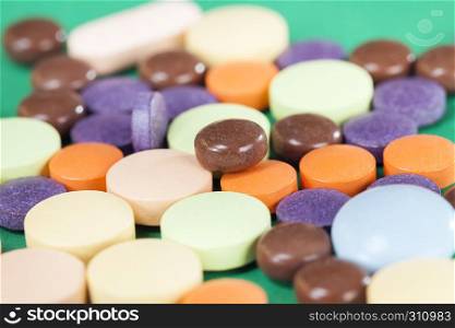 A large number of multi-colored tablets of different forms and purposes with different medical properties lying together in a heap on a green background. multi-colored tablets