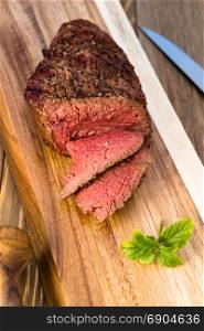 A large piece of grilled top sirloin sits on cutting board sliced and peppered