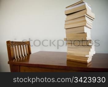 A large pile of books on a table with an empty chair