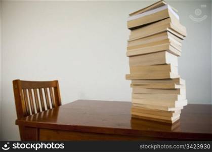 A large pile of books on a table with an empty chair