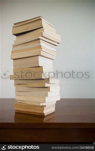 A large pile of books sits on a timber desktop with blank space behind
